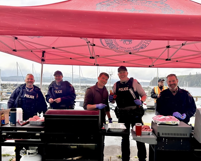 Des policiers en dessous d'une tente, cuisisant sur le BBQ