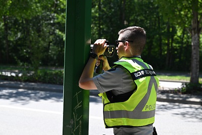 Un policier vêtu d’un gilet jaune réfléchissant utilise un radar de contrôle routier sur le bord d’une route.