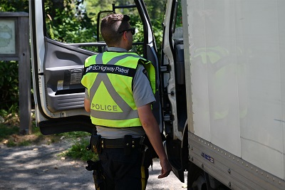 Un policier en uniforme jaune réfléchissant est accroupi à côté d’un camion utilitaire. 