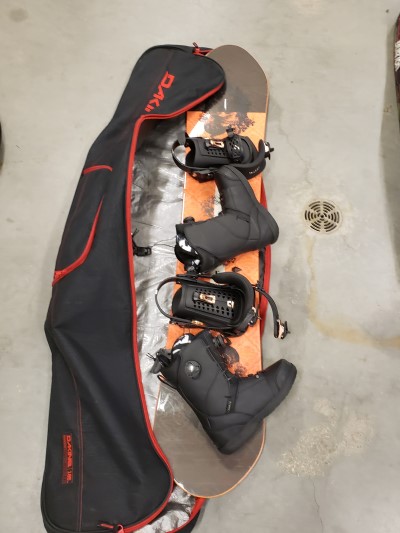 •	Snowboard two is an orange and black Lofi Rome snowboard with black boots and a black Dakine bag