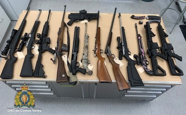 12 armes d’épaule et une arme de poing disposées sur une table. 