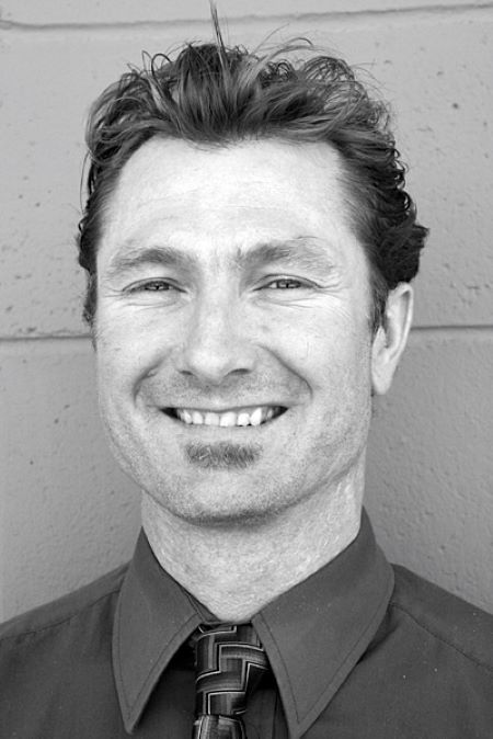 Photo en noir et blanc d’un homme de race blanche qui sourit et porte une chemise habillée et une cravate.
