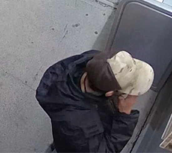 Suspect portant une veste noire à capuchon et une casquette de baseball camouflage brune et beige ainsi qu’un collier noir.