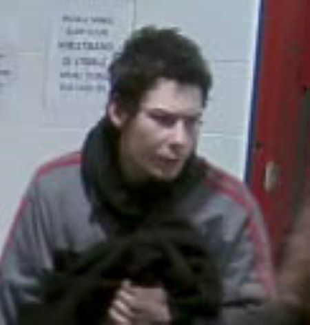 Visage du suspect : photo de face de la tête aux épaules d’un homme aux cheveux foncés, vêtu d’un blouson gris avec des rayures rouges. 