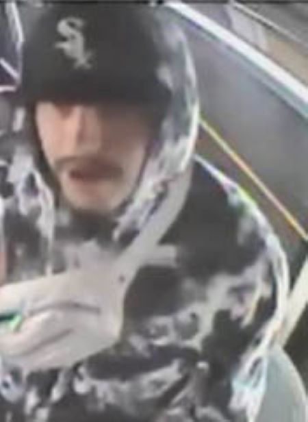 •	Suspect: A Caucasian man in his 20s with a dark, thick moustache, is wearing a black WhiteSox cap. The hood of his white camo sweater is pulled up over the cap, and a cross-body fanny-pack with green zipper flies is across his upper body. 